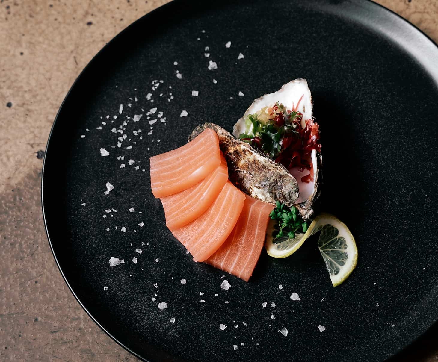 bluu seafood cultivated salmon served on a black plate with lemon rinds