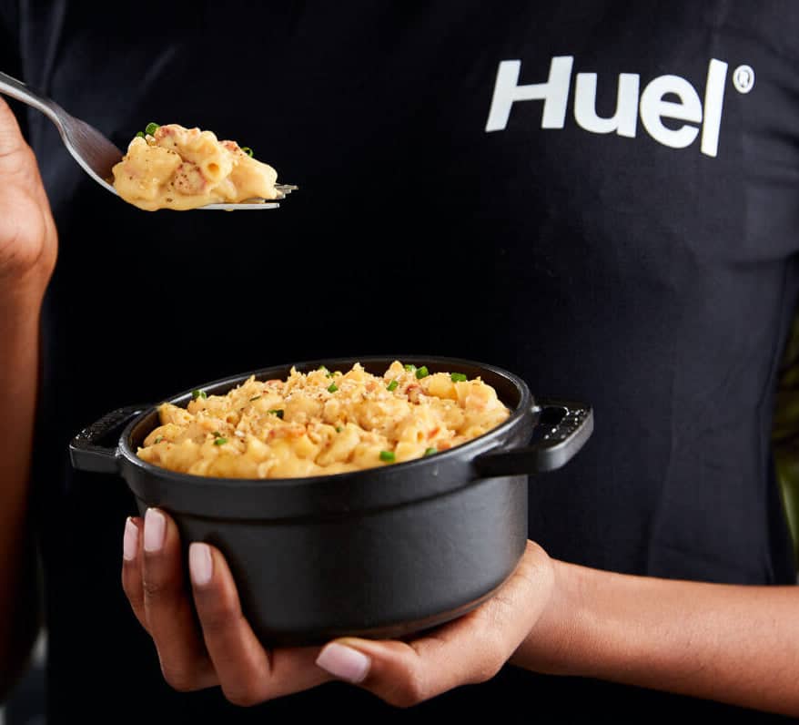 a woman holding a bowl with huel's ready to cook nutritional pasta