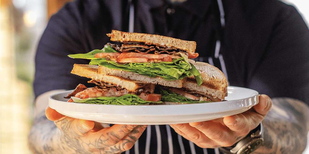 a mycelium bacon sandwich on a plate held by a man