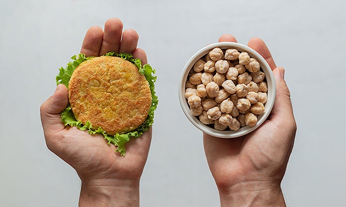 A person holding in one hand whole chickpeas and on the other a chickpea burger. 