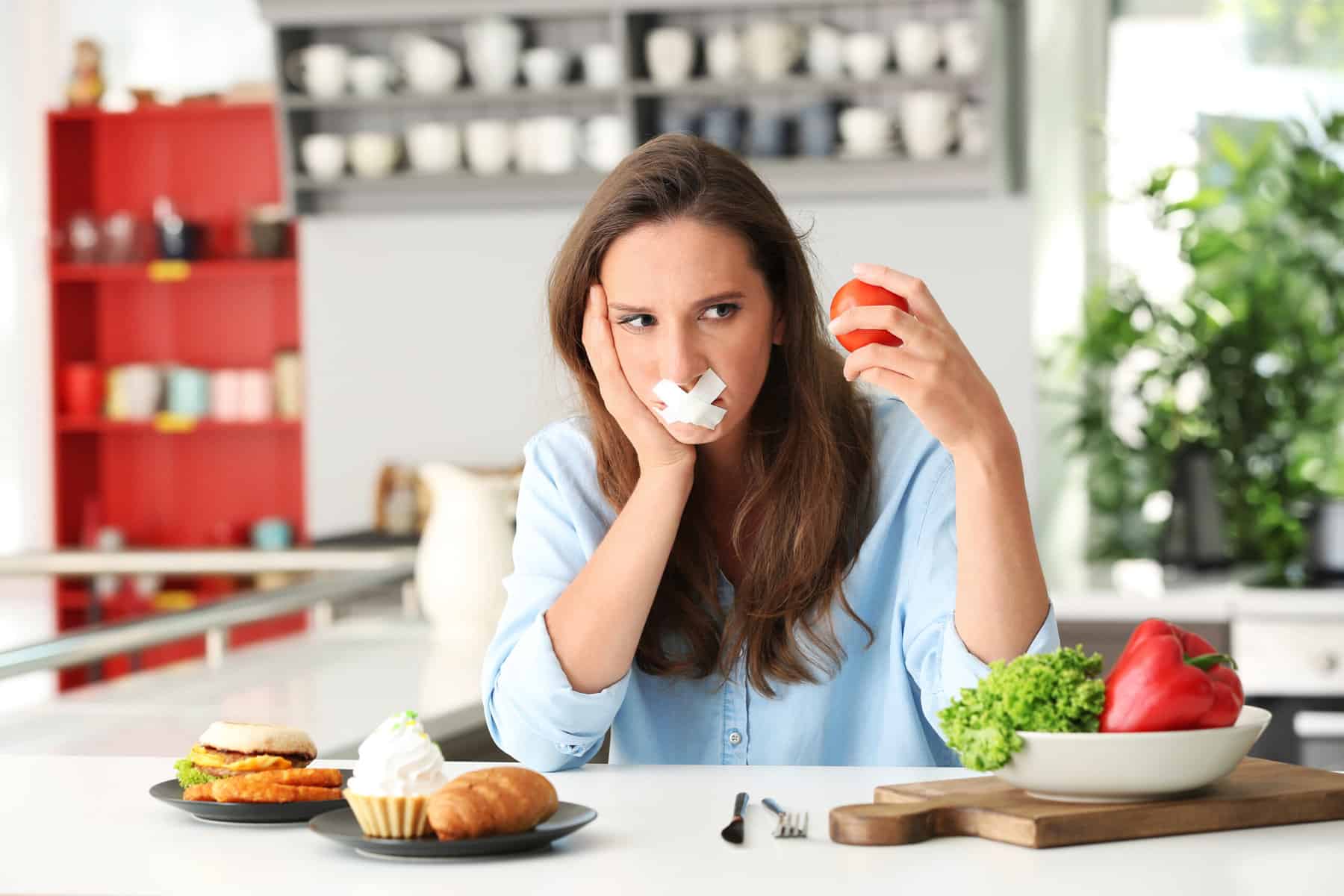 Woman with taped mouth and different products in kitchen.