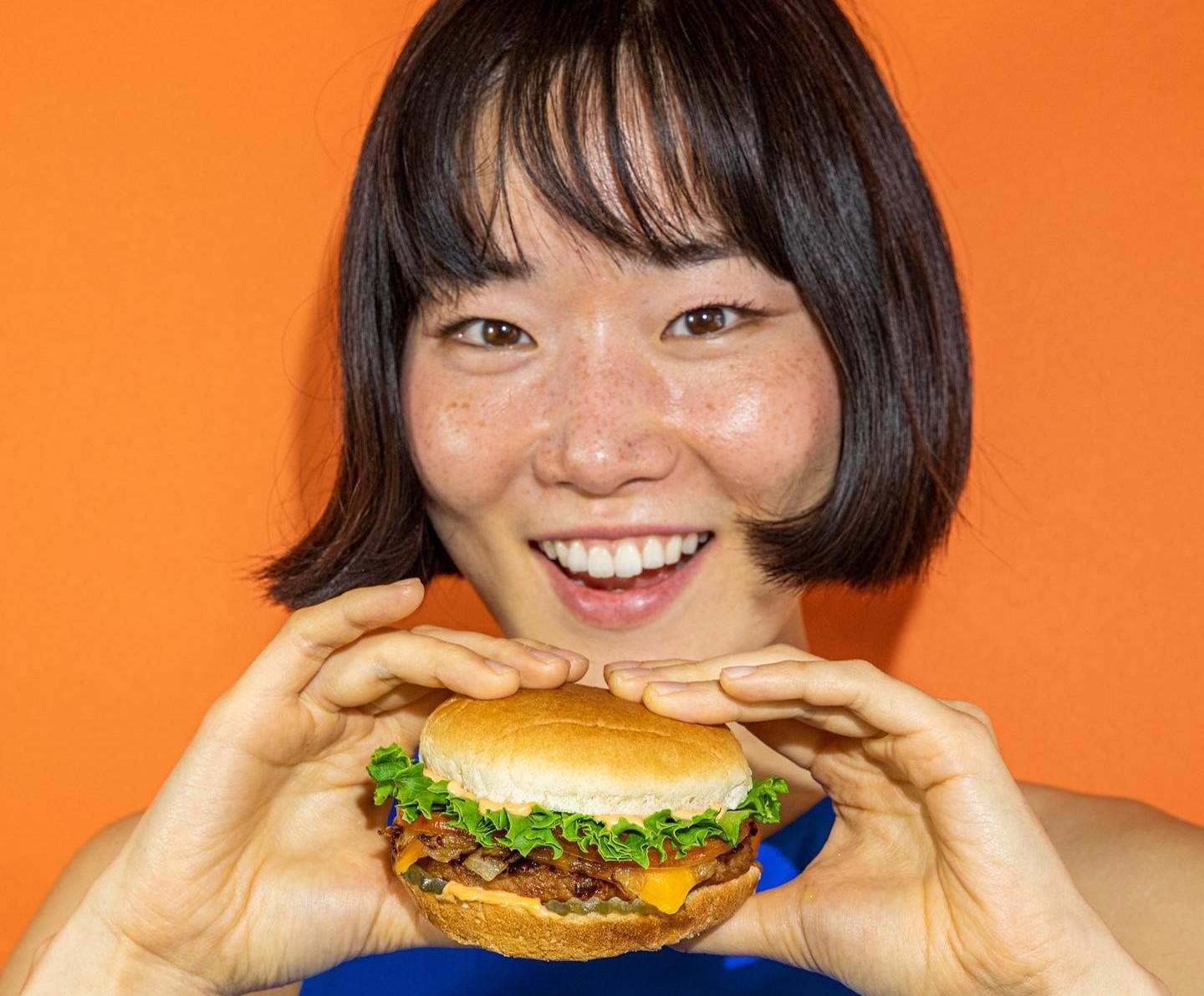 Vegan fast food market chain plant power's cheeseburger being held by a smiling woman